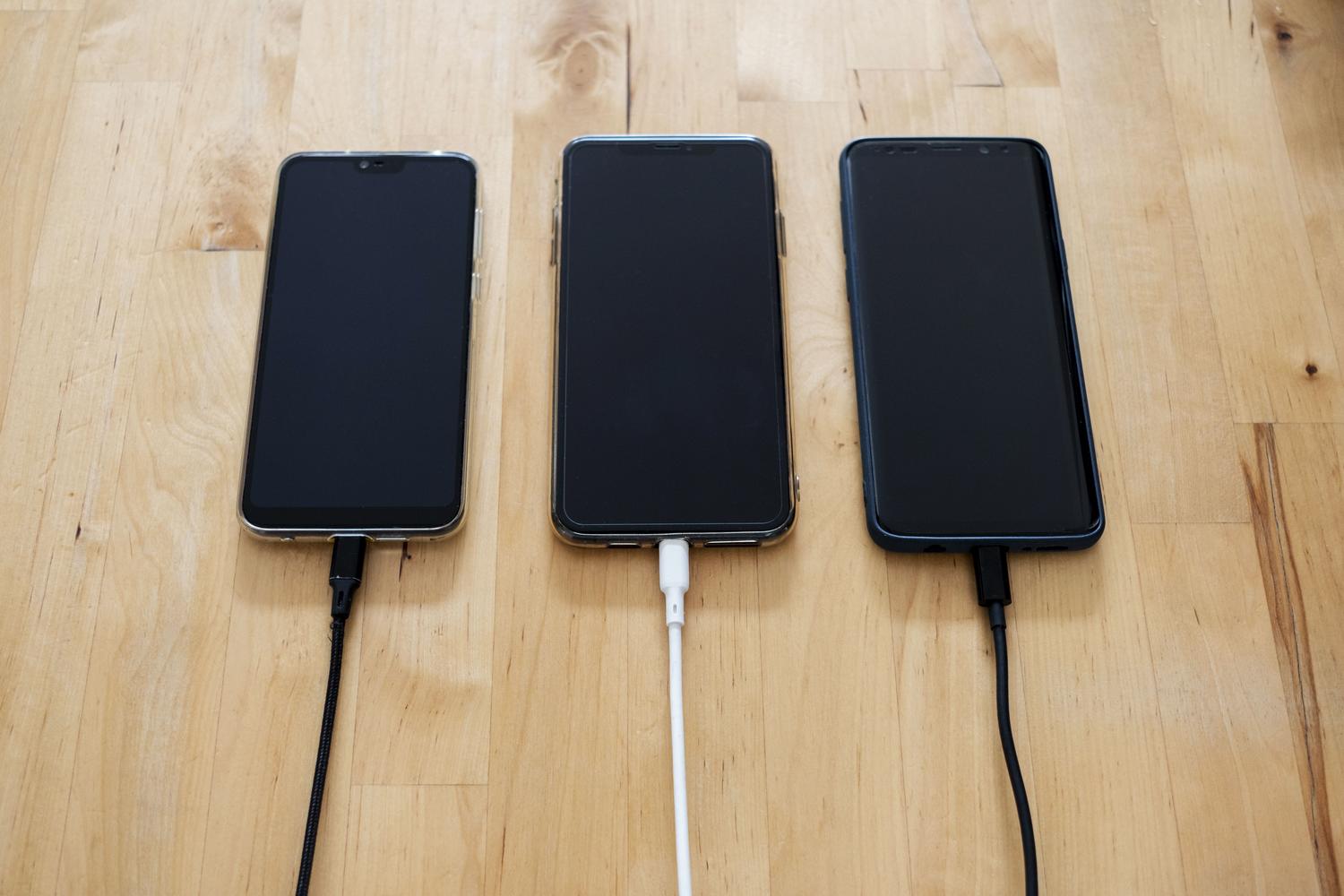 Varios smartphones Android conectados a sus cargadores sobre una mesa de madera, representando la carga térmica de la batería.