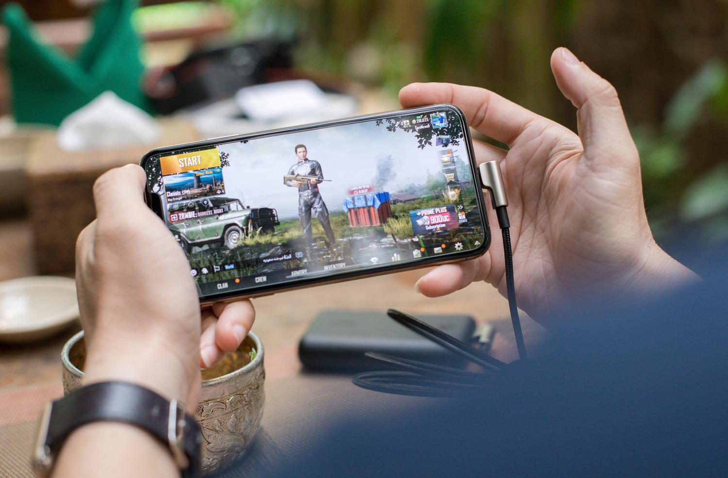 Persona jugando a un videojuego exigente en un smartphone mientras el dispositivo está conectado al cargador.