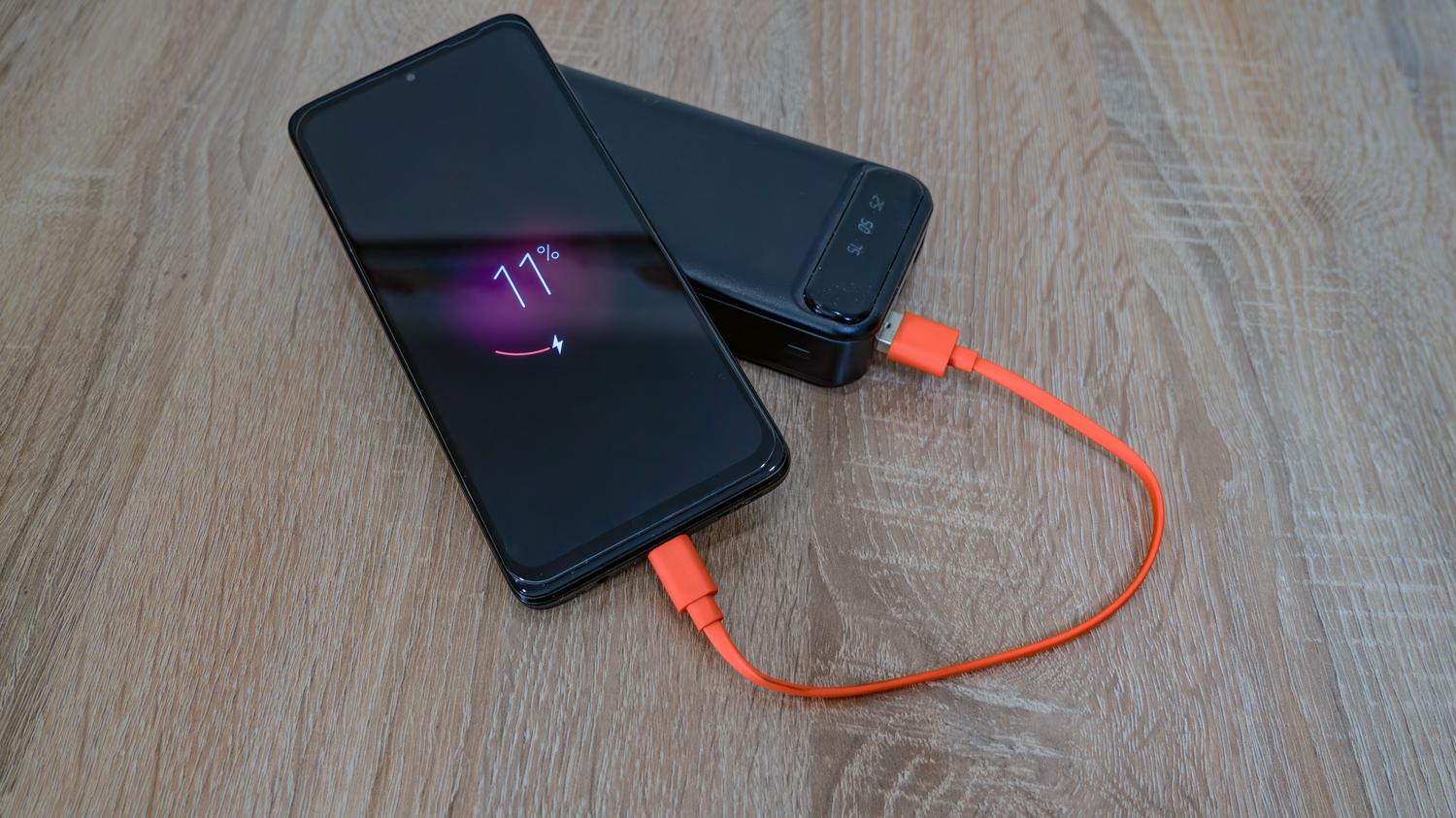 Smartphone conectado a una batería externa (power bank) sobre una mesa de madera, ideal para ilustrar soluciones de autonomía en movimiento.