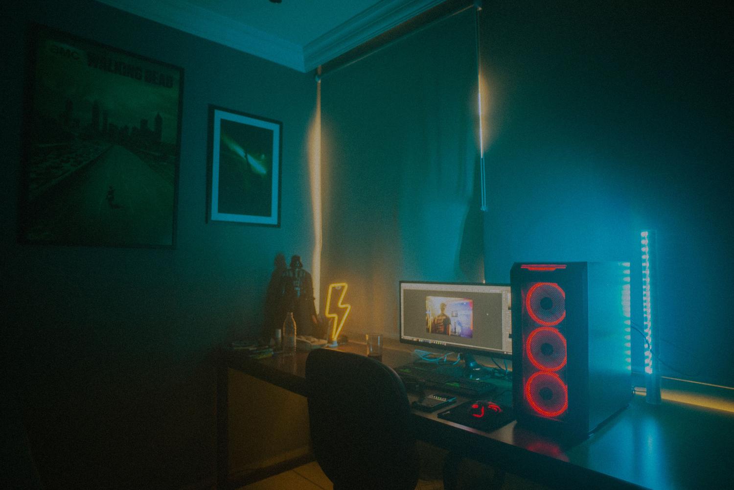 Atmospheric gaming room featuring a desktop computer with RGB fans and neon ambient lighting.