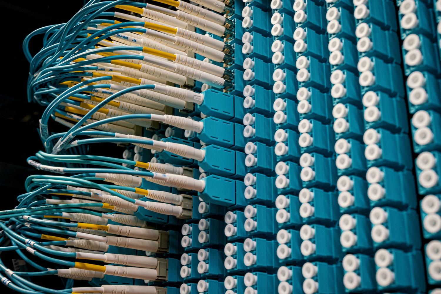 Panel de parcheo de fibra óptica con cables cian, ilustrando la transmisión de datos a alta velocidad y la complejidad física de las redes.