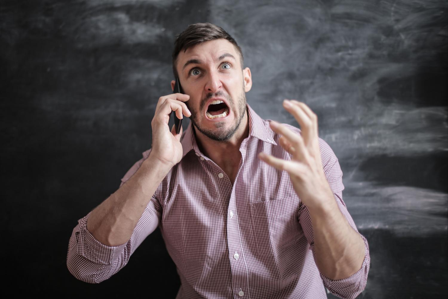 Hombre frustrado intentando usar un teléfono móvil que no responde