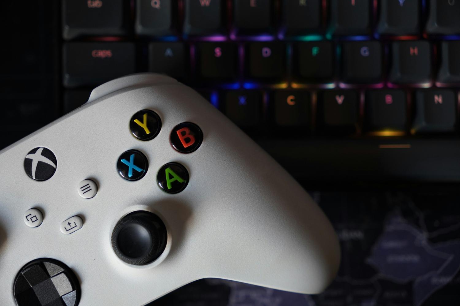 Mando de Xbox blanco junto a un teclado mecánico con iluminación RGB en un ambiente oscuro