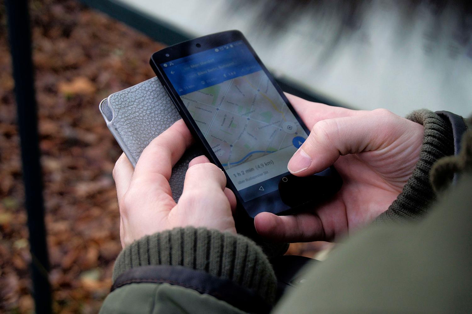Primer plano de manos operando una aplicación de mapas en un smartphone al aire libre, capturando el momento de decisión del usuario local.