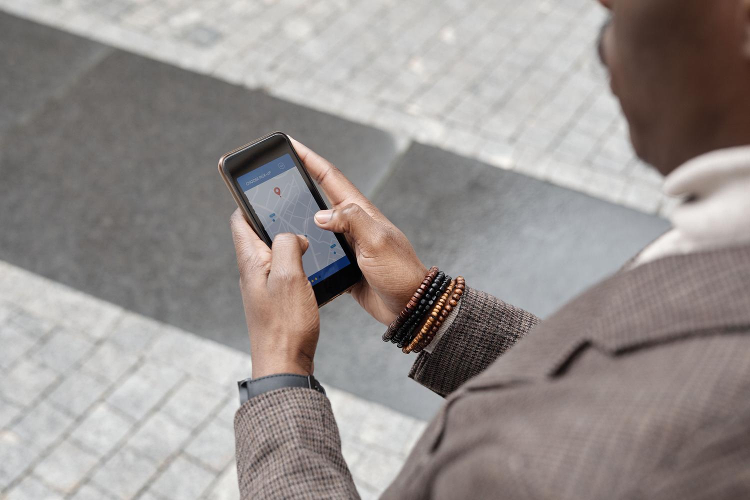 Persona profesional utilizando una aplicación de navegación en su smartphone mientras camina por una calle de la ciudad, ilustrando la intención de búsqueda geográfica.