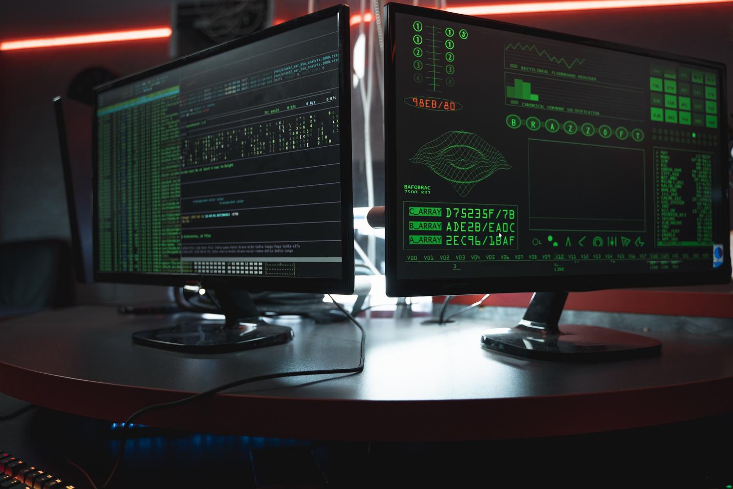 Pantallas de ordenador en un entorno oscuro mostrando interfaces de programación y código fuente, representando el software de los sistemas operativos.