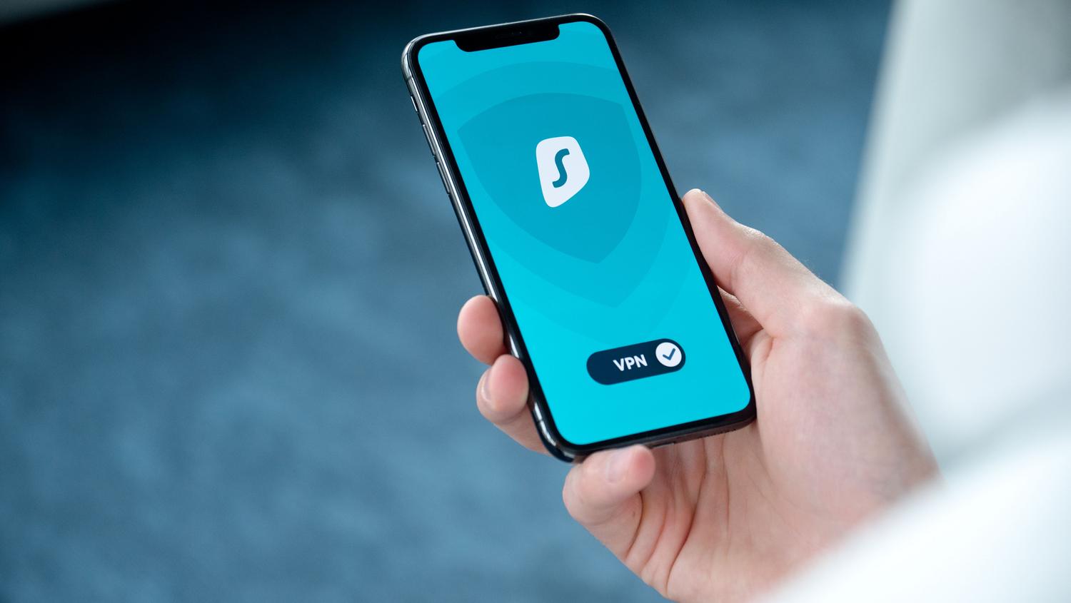 Mano sosteniendo un iPhone con un escudo de seguridad en pantalla, representando la protección de la privacidad y el uso de VPN.