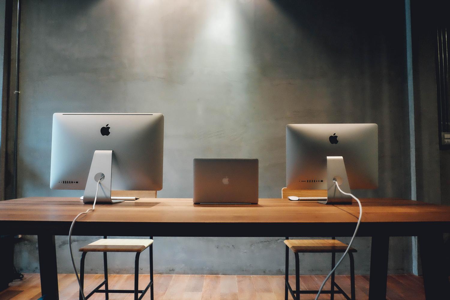 Flota de computadoras iMac idénticas en un espacio de trabajo corporativo moderno.