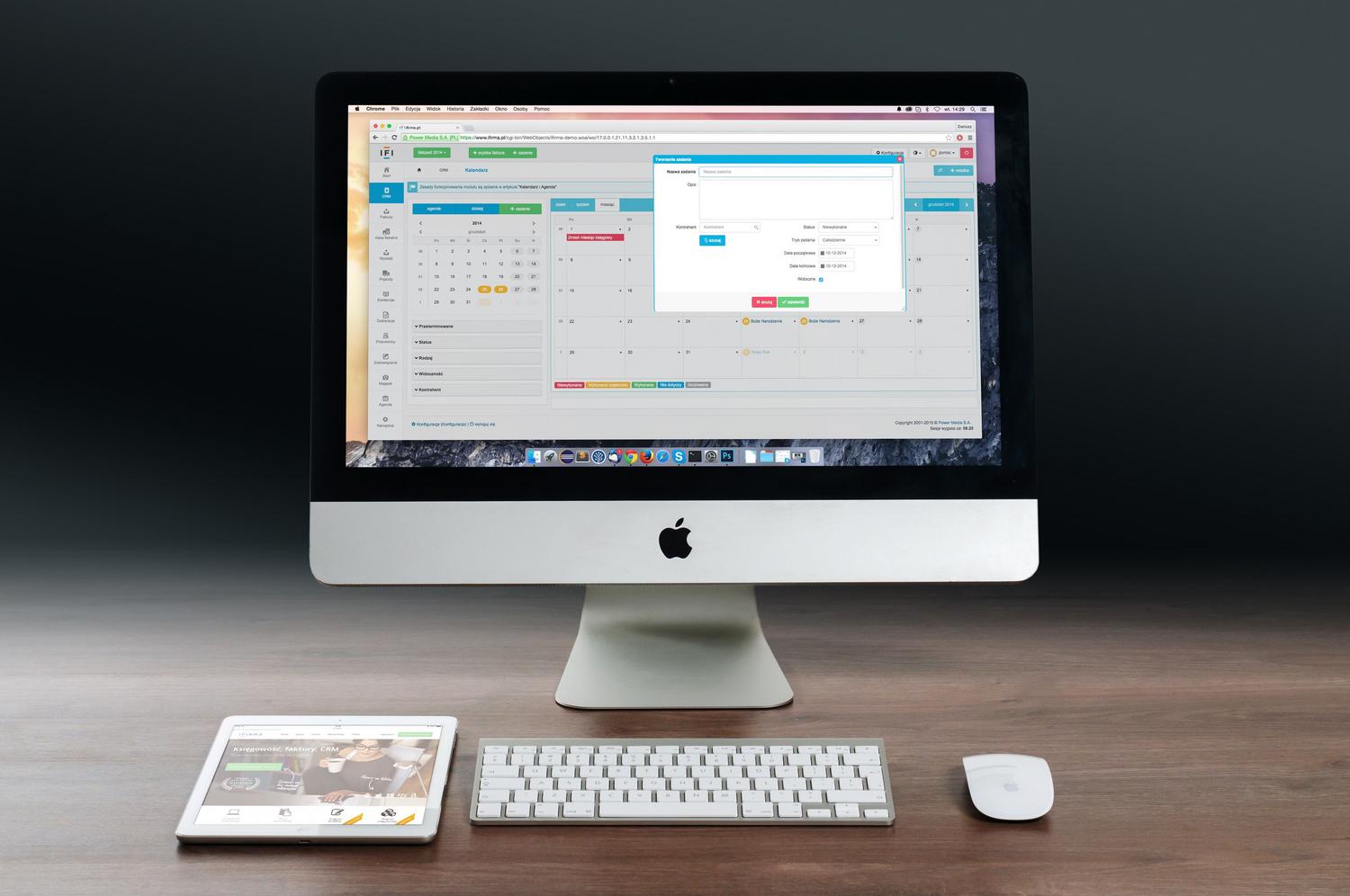 Estación de trabajo con iMac y iPad mostrando software de gestión empresarial en una oficina moderna.