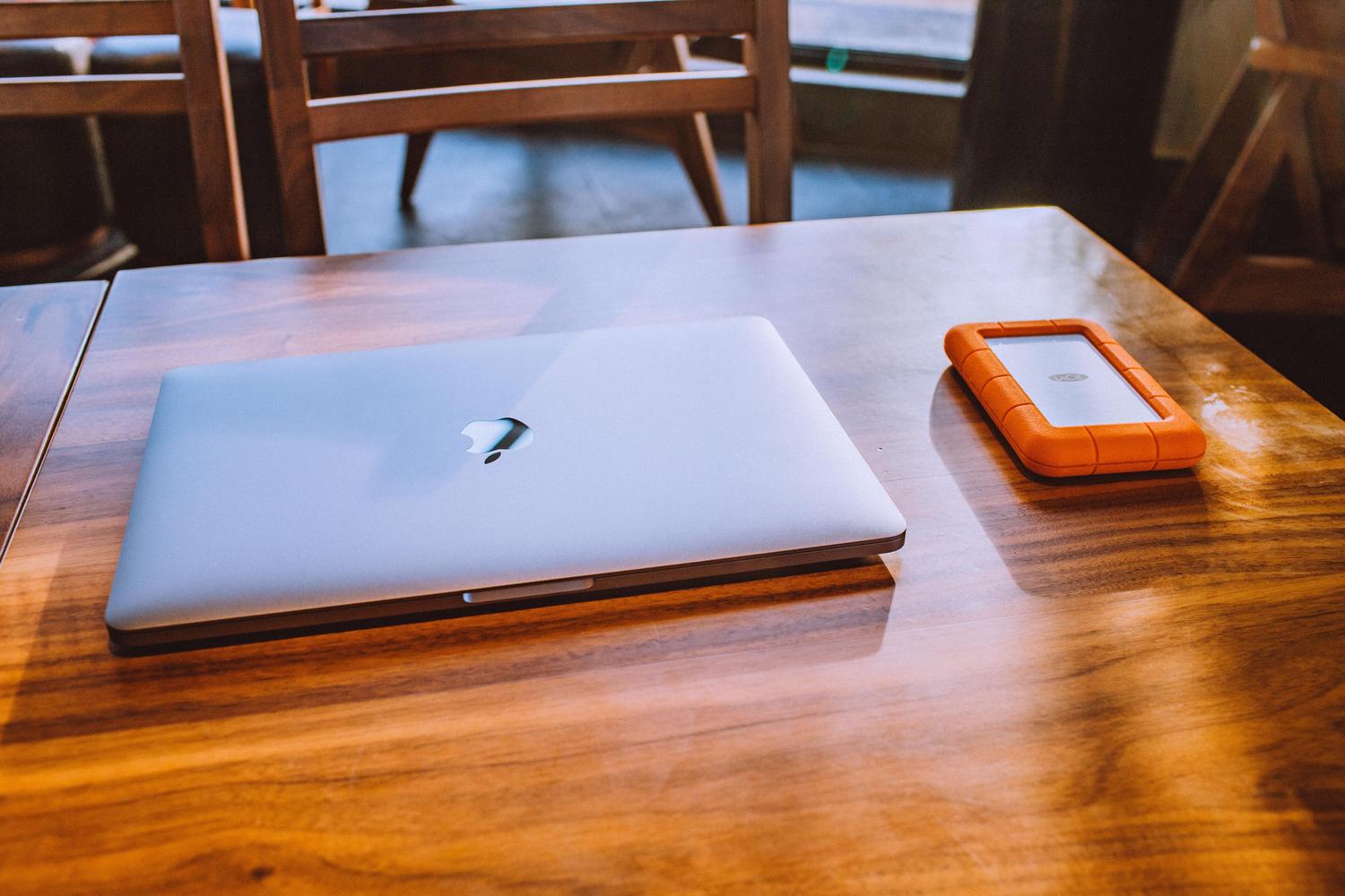 MacBook y disco duro externo rugerizado sobre una mesa de madera, simbolizando la seguridad de las copias de seguridad y Time Machine.