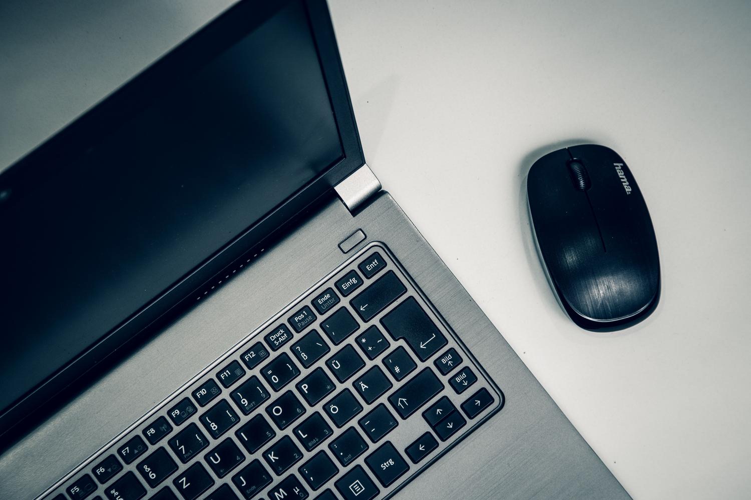 Detalle de un MacBook plateando y un ratón inalámbrico negro sobre un escritorio blanco