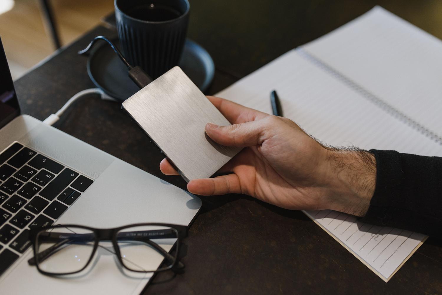Persona conectando un disco duro externo a un ordenador portátil en un entorno de trabajo profesional, ideal para la revisión de conectividad.