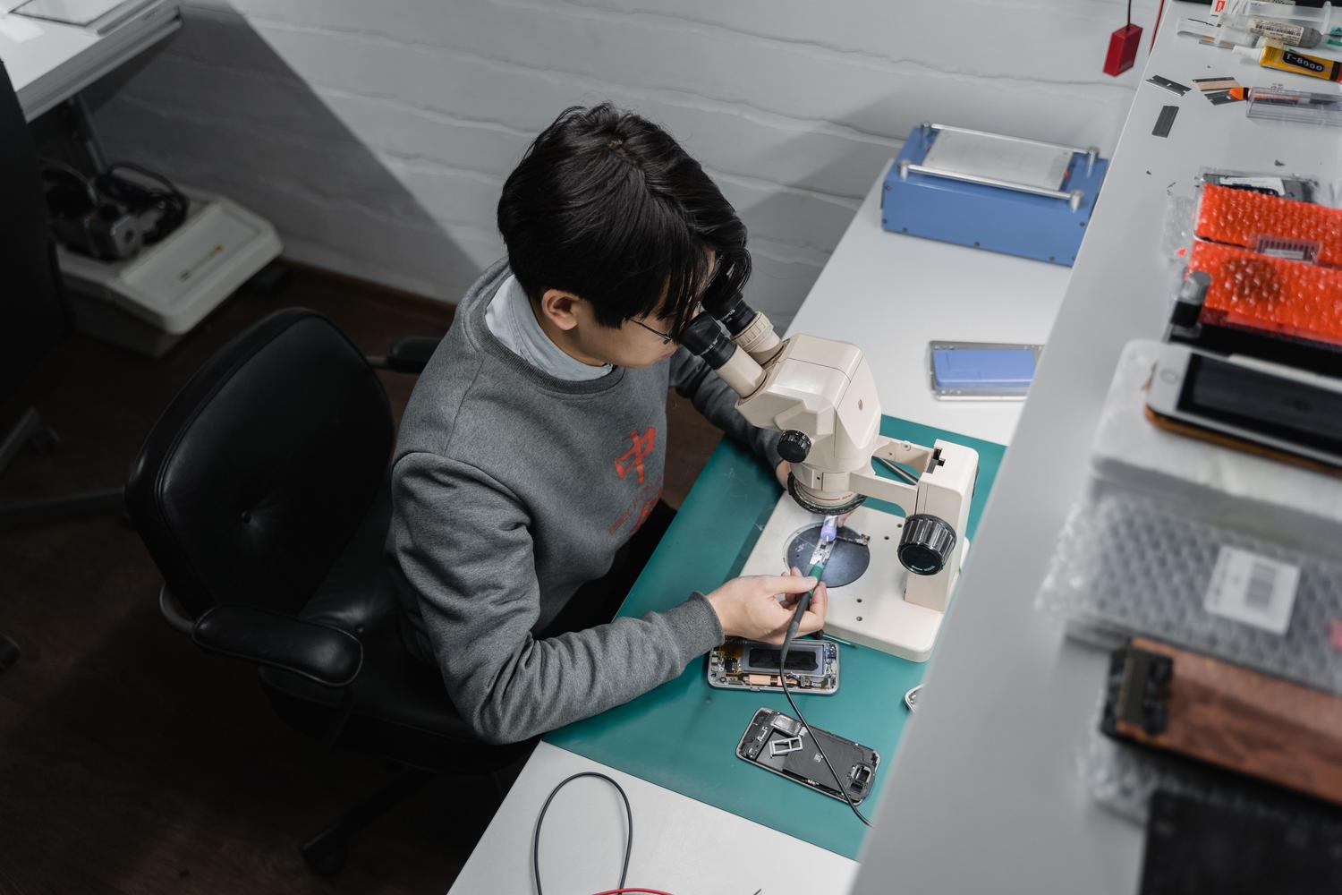 Técnico especializado trabajando en la reparación de un smartphone bajo un microscopio, ideal para la sección de microsoldadura y fallos físicos.