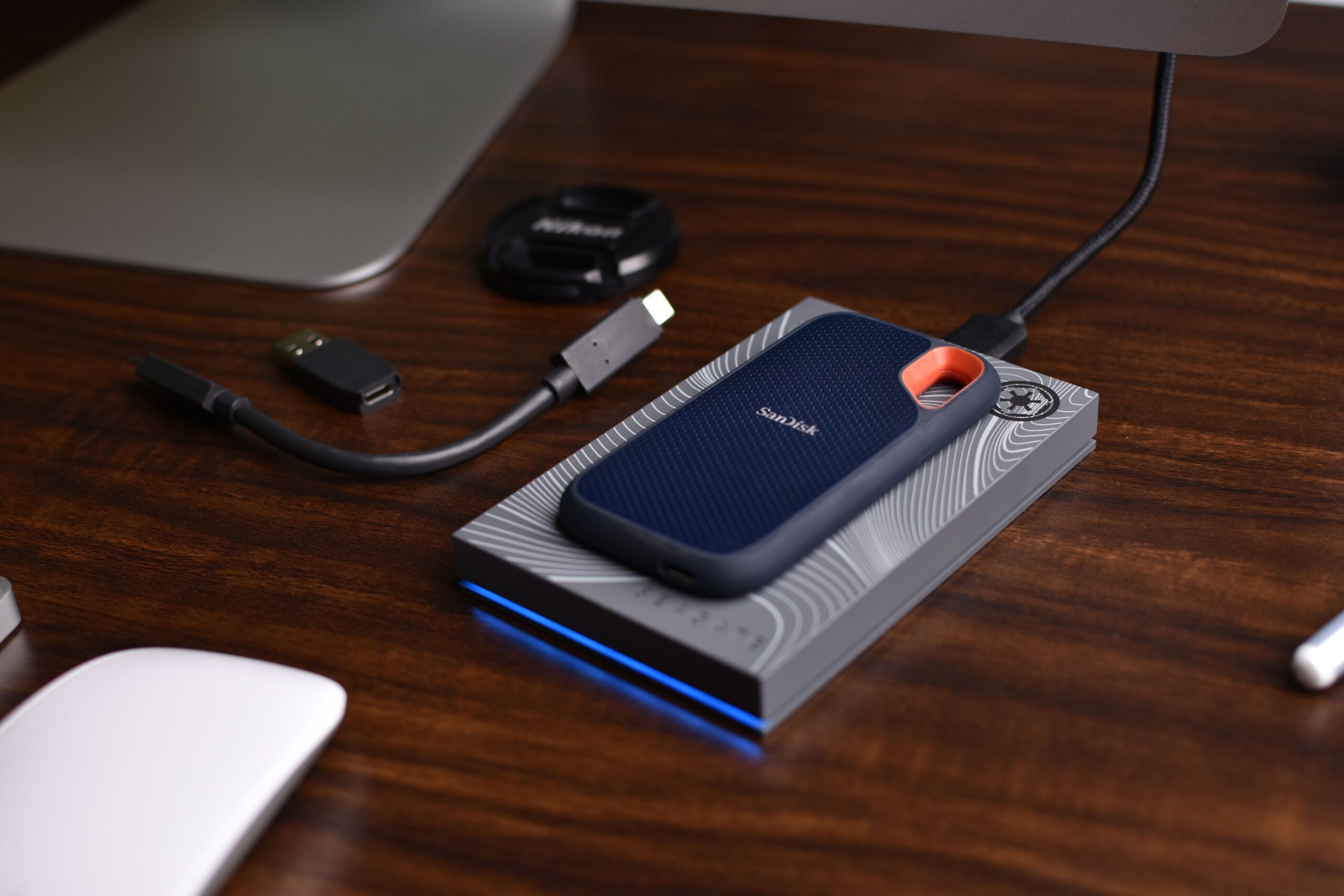 Unidad SSD portátil SanDisk con accesorios USB sobre una mesa de madera, ideal para ilustrar la gestión de unidades externas y tarjetas SD.