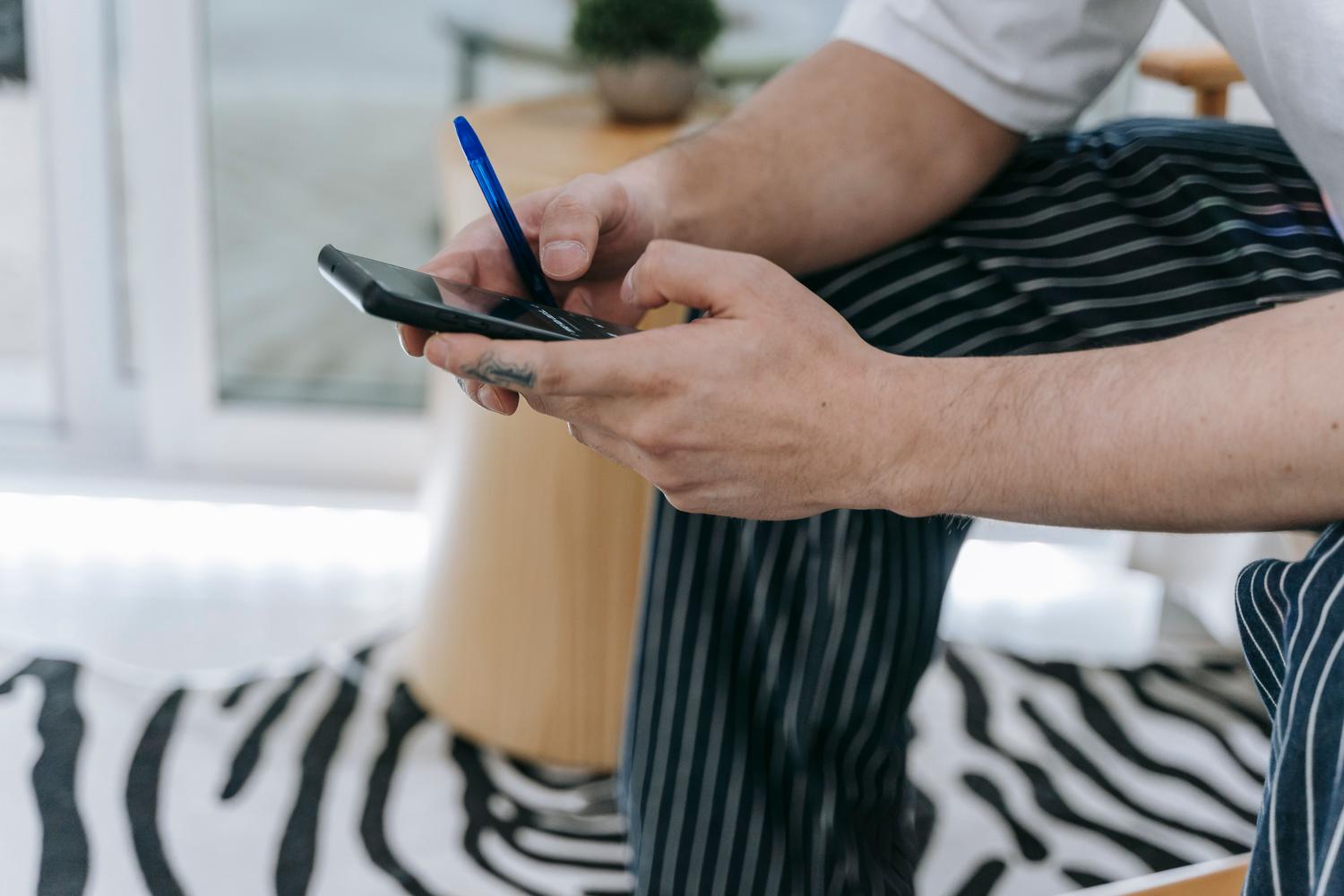 Persona utilizando un smartphone y un bolígrafo, representando la productividad y la gestión de información multitarea. Persona utilizando un smartphone y un bolígrafo, representando la productividad y la gestión de información multitarea.