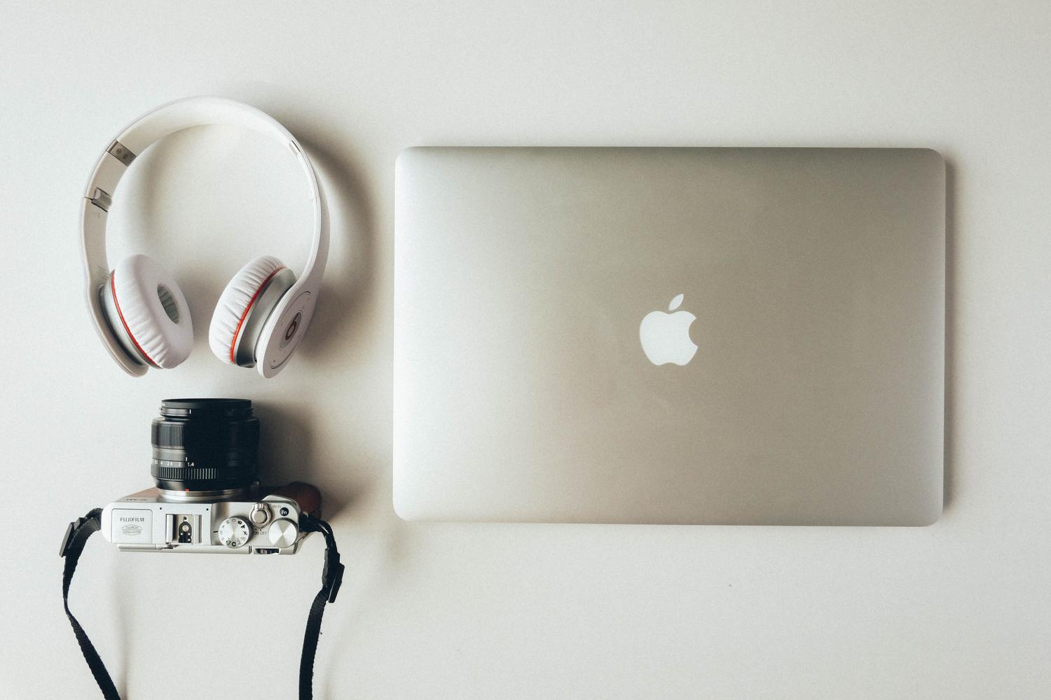 Composición plana de un MacBook, auriculares y una cámara, sugiriendo un espacio de trabajo para profesionales creativos.