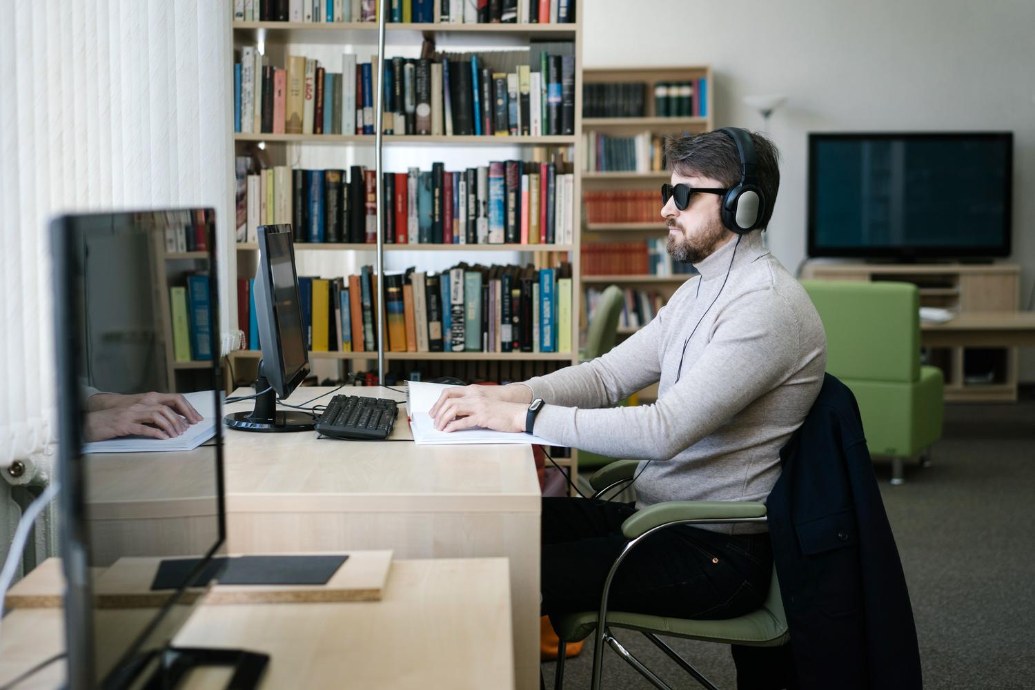 Hombre con discapacidad visual usando auriculares y una línea Braille con un ordenador, ilustrando el uso de VoiceOver en macOS.