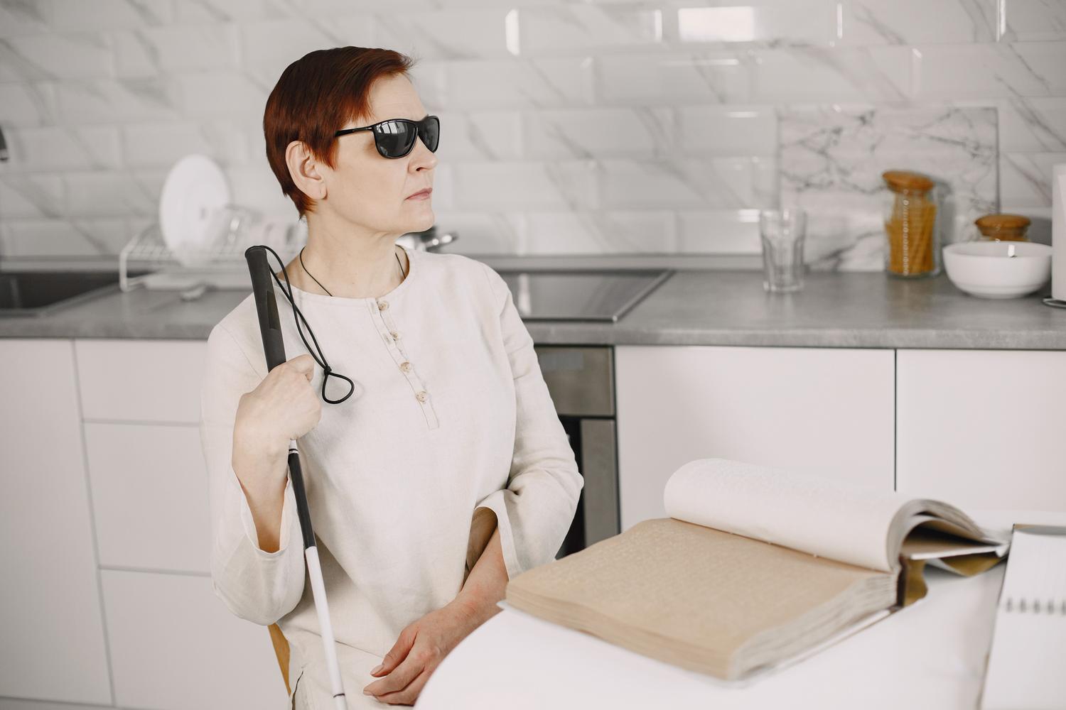 Mujer con discapacidad visual con bastón blanco y libro Braille, representando la diversidad de usuarios con visión reducida.