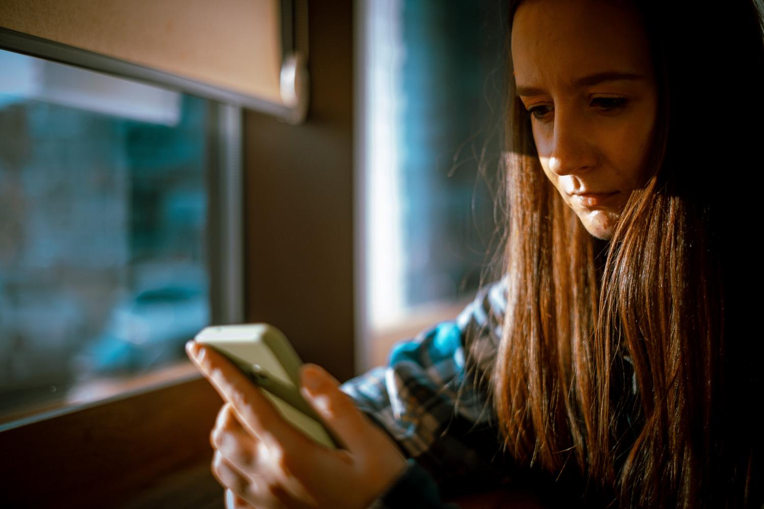 Mujer joven utilizando su teléfono móvil con luz natural entrando por una ventana