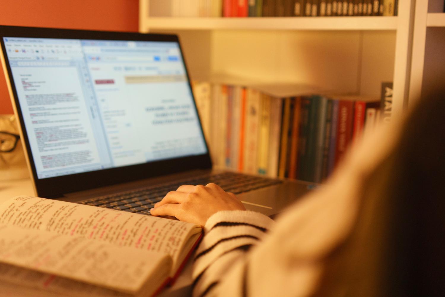 Persona utilizando un portátil y un libro abierto en un ambiente tranquilo de estudio, ideal para ilustrar la lectura de documentos PDF.