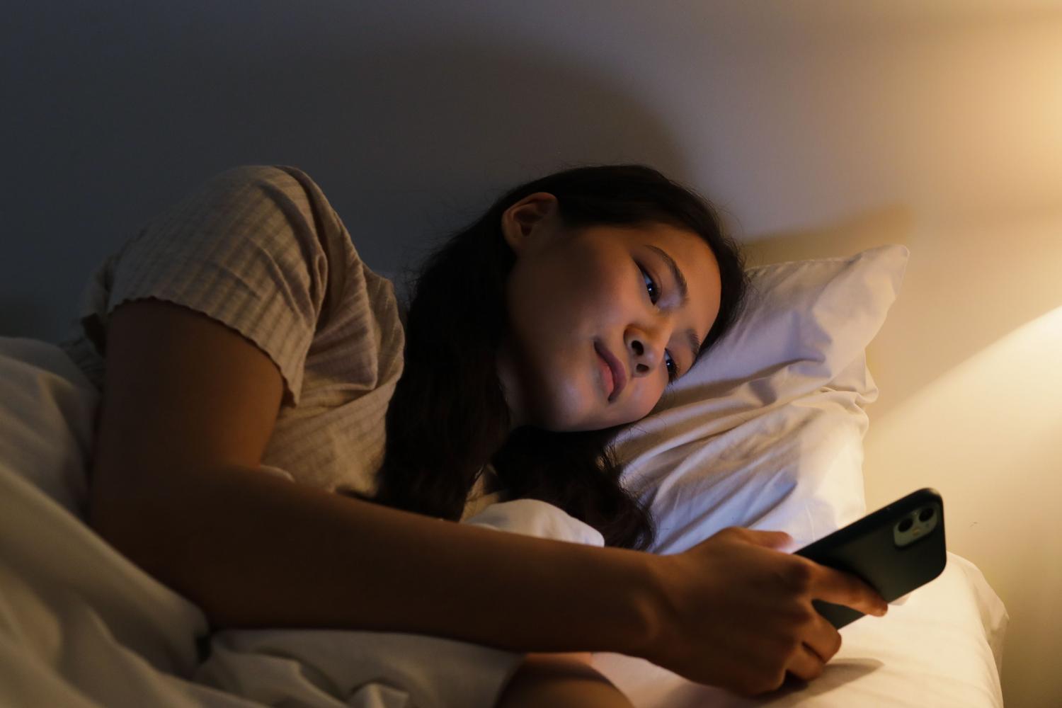 Persona utilizando el teléfono móvil en la cama con iluminación cálida, representando el uso de filtros de luz azul y modo protección ocular.