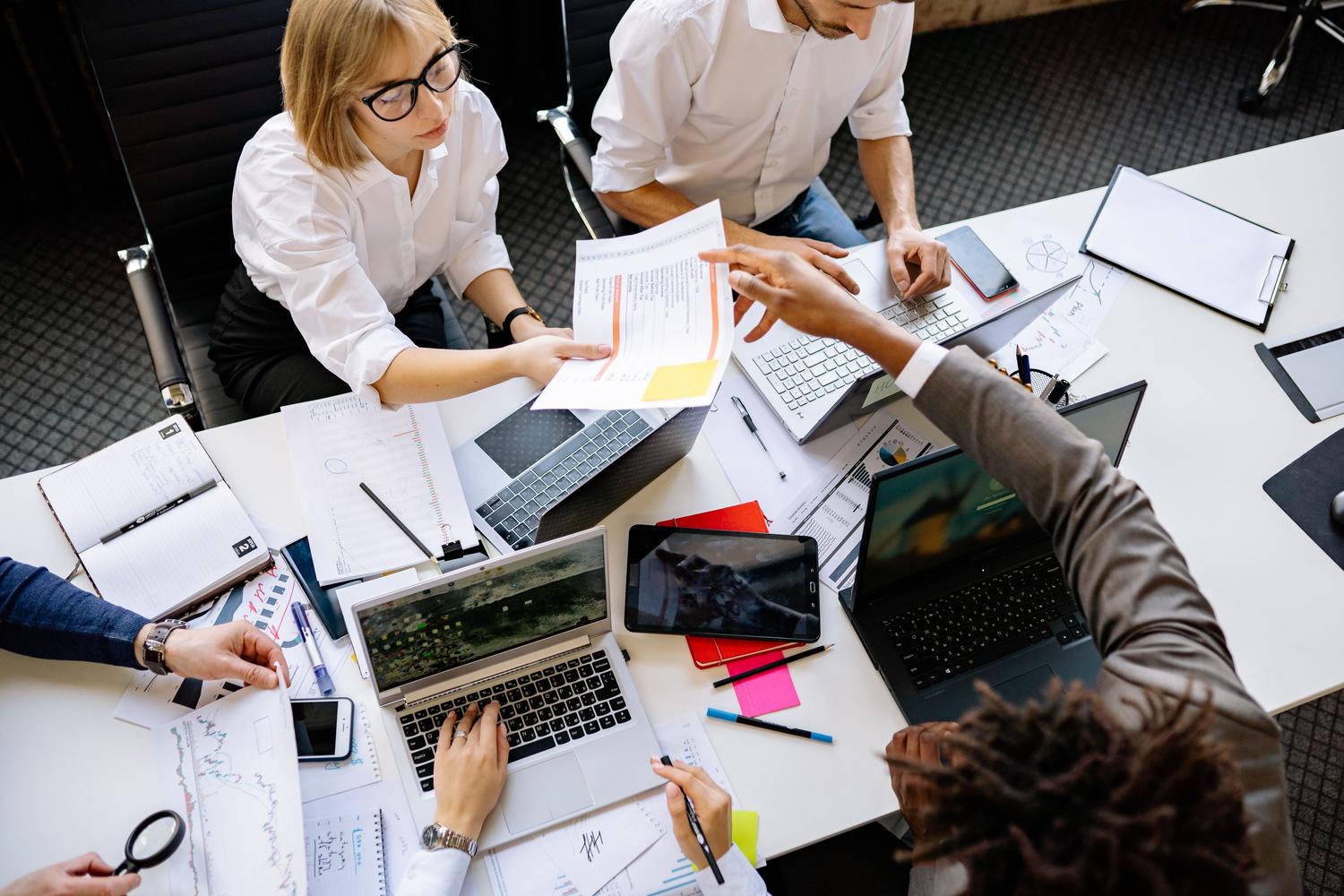 Equipo profesional colaborando en una mesa de oficina con portátiles, gráficos y documentos, representando la gestión de proyectos complejos y flujos de trabajo coordinados. Equipo profesional colaborando en una mesa de oficina con portátiles, gráficos y documentos, representando la gestión de proyectos complejos y flujos de trabajo coordinados.