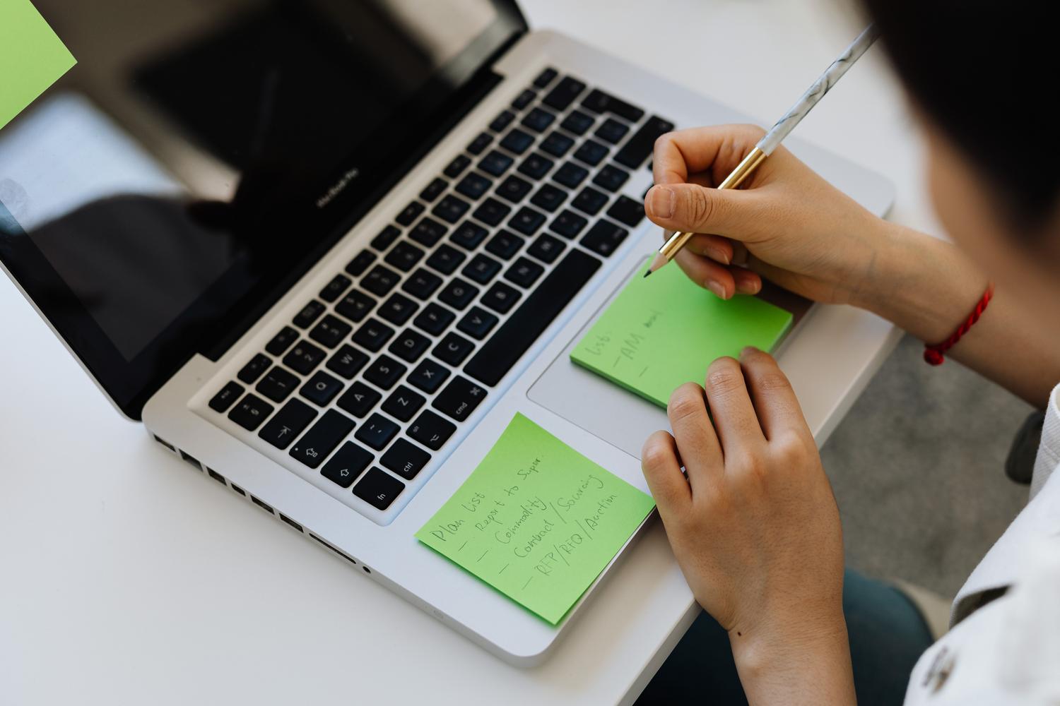 Persona organizando tareas en notas adhesivas verdes junto a un portátil, simbolizando la captura rápida de ideas y el diseño de sistemas de productividad. Persona organizando tareas en notas adhesivas verdes junto a un portátil, simbolizando la captura rápida de ideas y el diseño de sistemas de productividad.