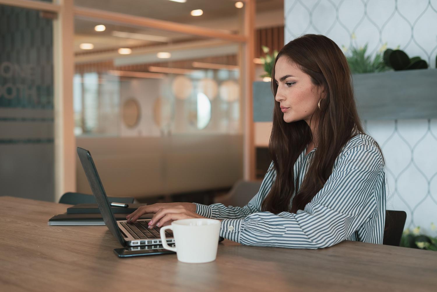 Mujer profesional concentrada trabajando en su ordenador portátil en una oficina moderna y luminosa, representando la ejecución eficiente de tareas.