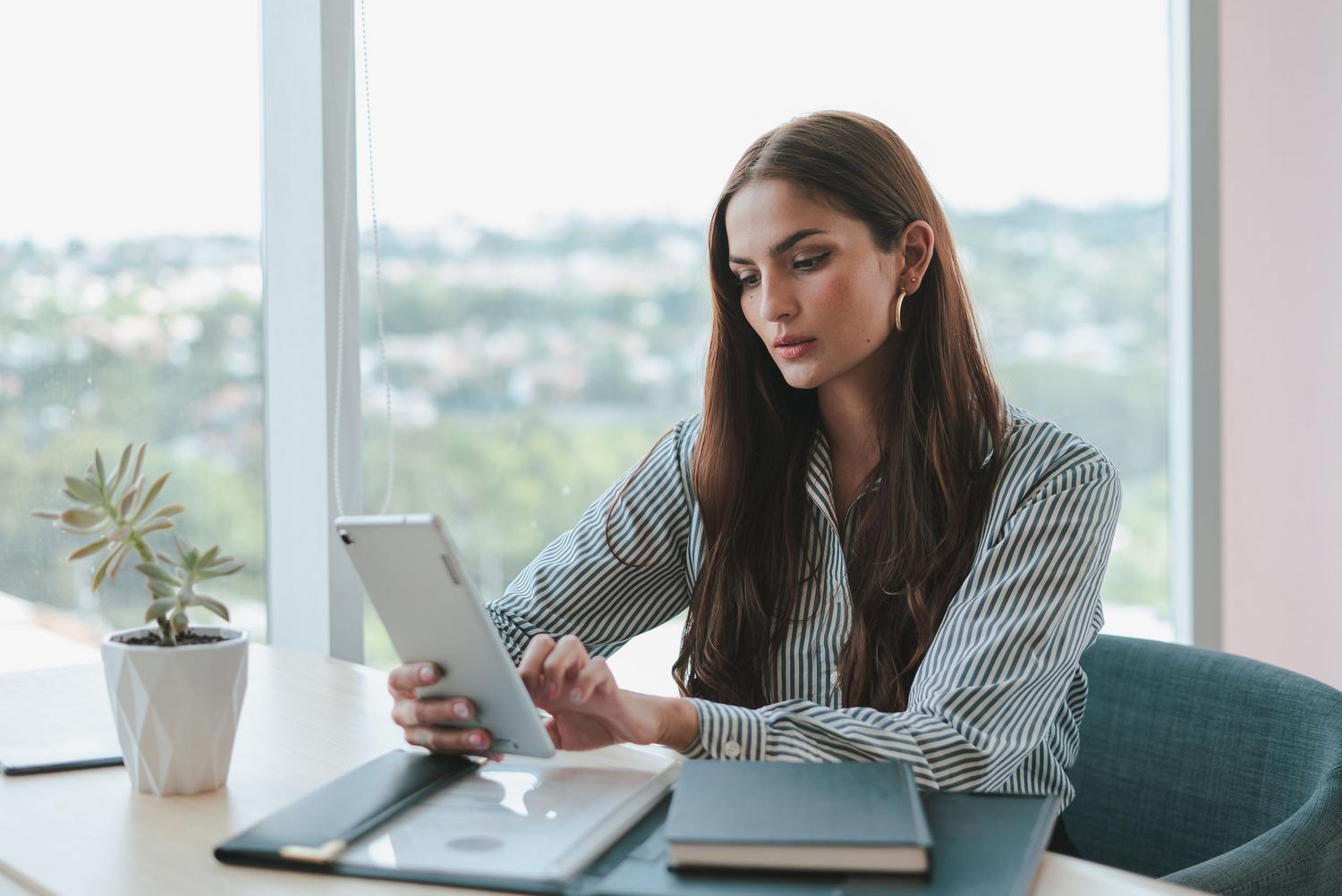 Mujer de negocios utilizando una tablet en un escritorio organizado, reflejando la gestión profesional y la revisión de resultados optimizados.