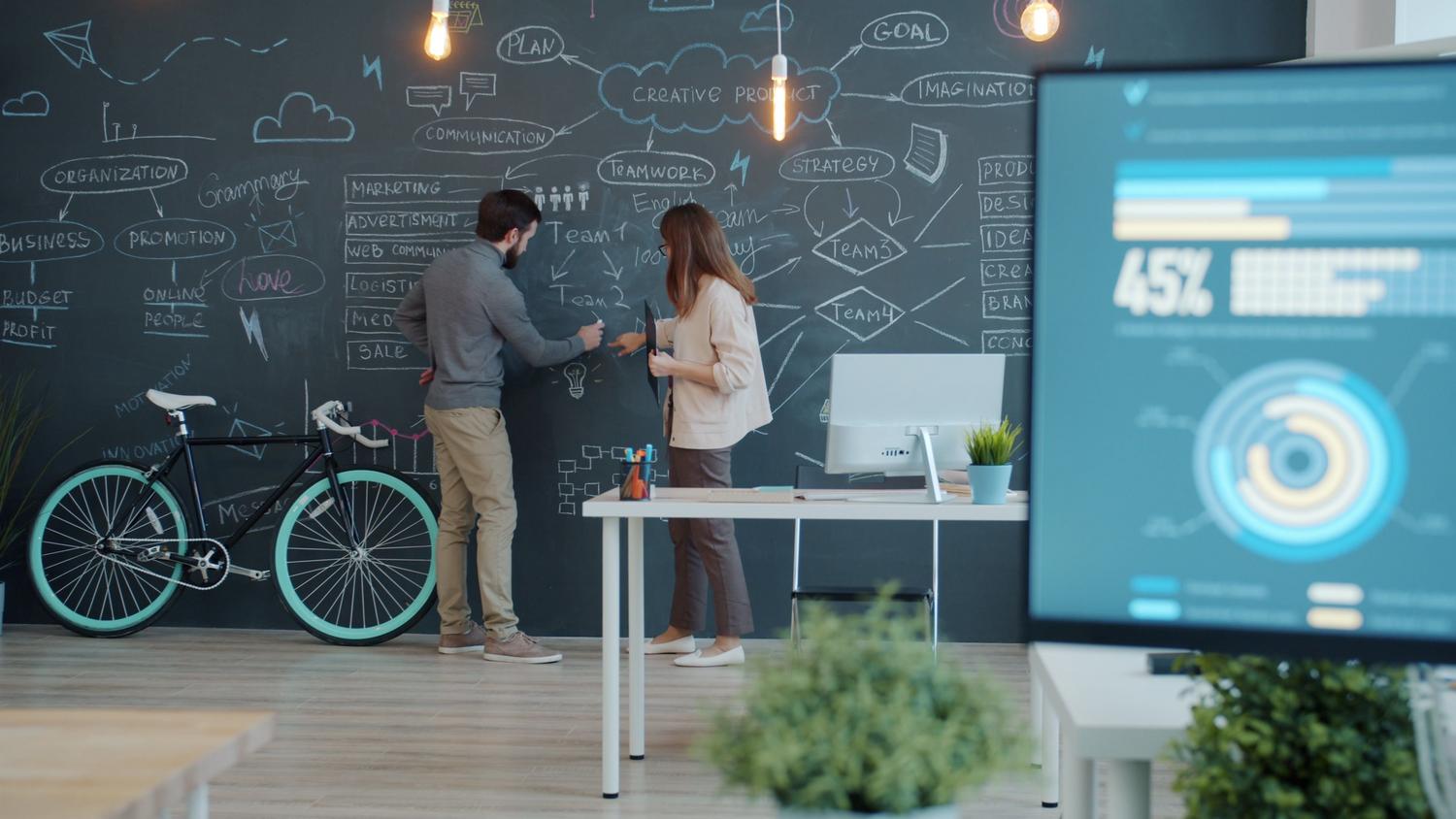 Dos profesionales colaborando en una sesión de brainstorming frente a una pizarra con un mapa mental complejo, ilustrando la detección de procesos y definición de estrategias.