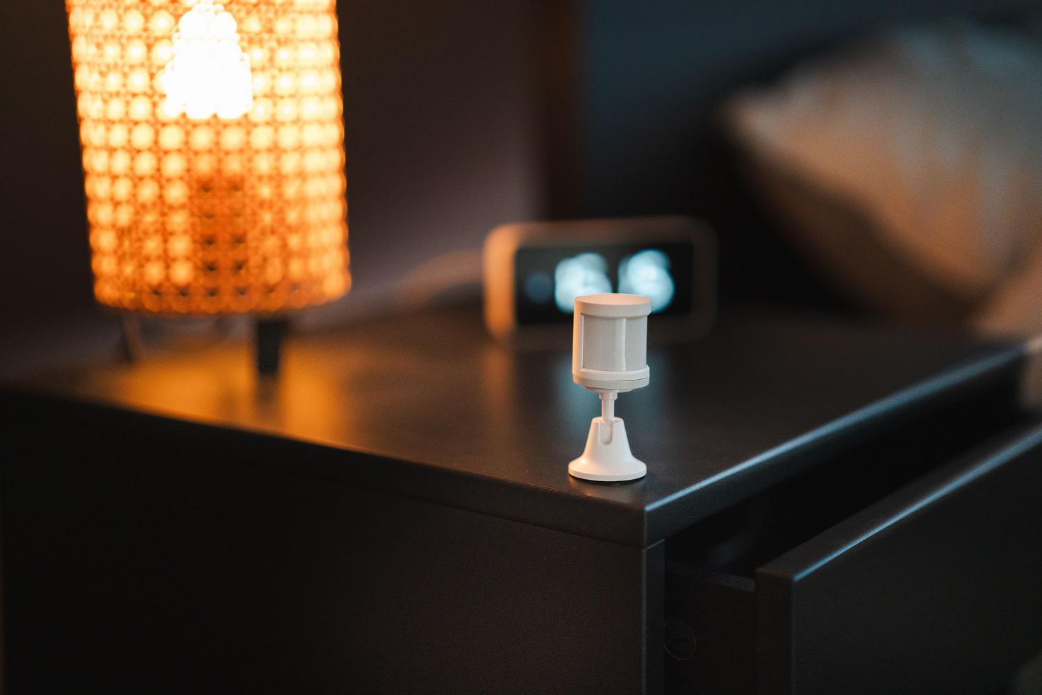 Sensor de movimiento inteligente instalado en una mesa de noche junto a una lámpara en un dormitorio moderno.
