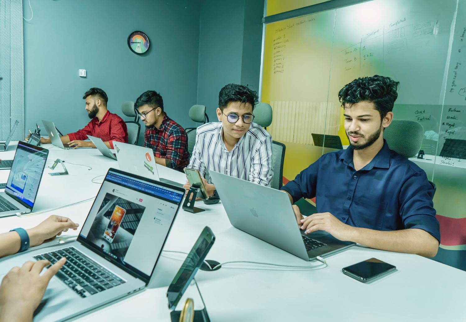 Grupo de jóvenes profesionales trabajando en equipo en un espacio de coworking moderno con portátiles y pizarras de planificación