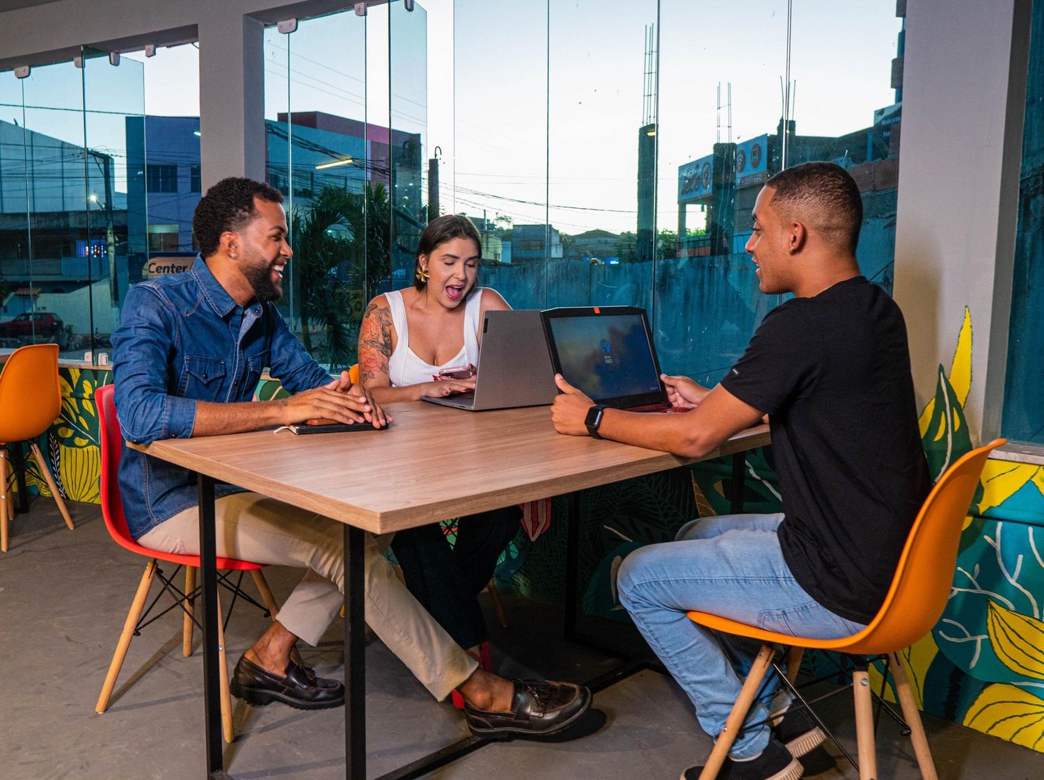 Equipo de trabajo multidisciplinar colaborando con ordenadores portátiles en un espacio de oficina urbano y luminoso