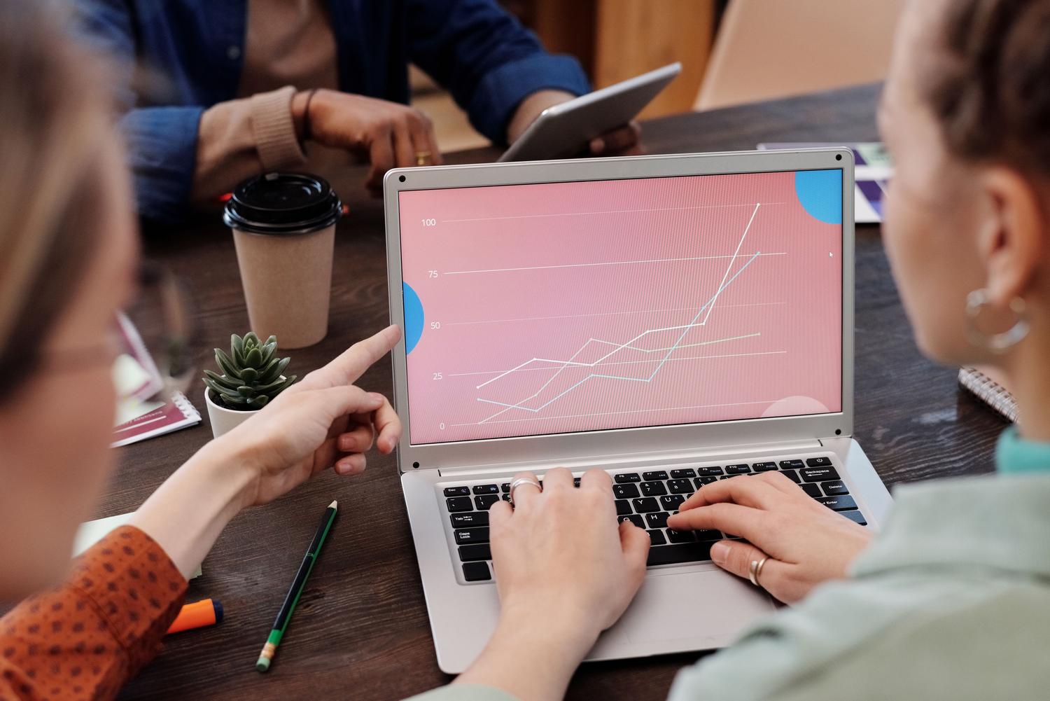 Profesionales colaborando en tiempo real analizando gráficas de datos en un portátil en una oficina moderna