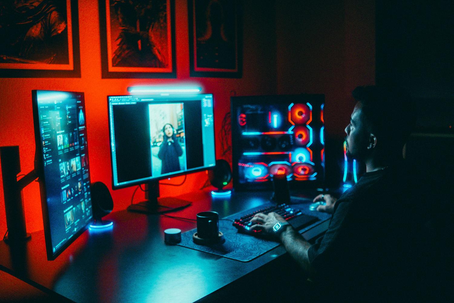 Un joven desarrollador trabajando en un setup de computadora con múltiples pantallas y luces neon, representando el entorno de creación de videojuegos.