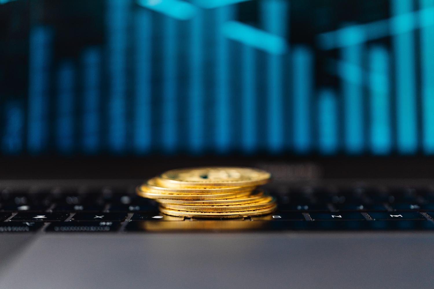 Monedas de oro sobre un teclado de computadora con un gráfico de crecimiento en pantalla, simbolizando la monetización y el éxito financiero del juego.