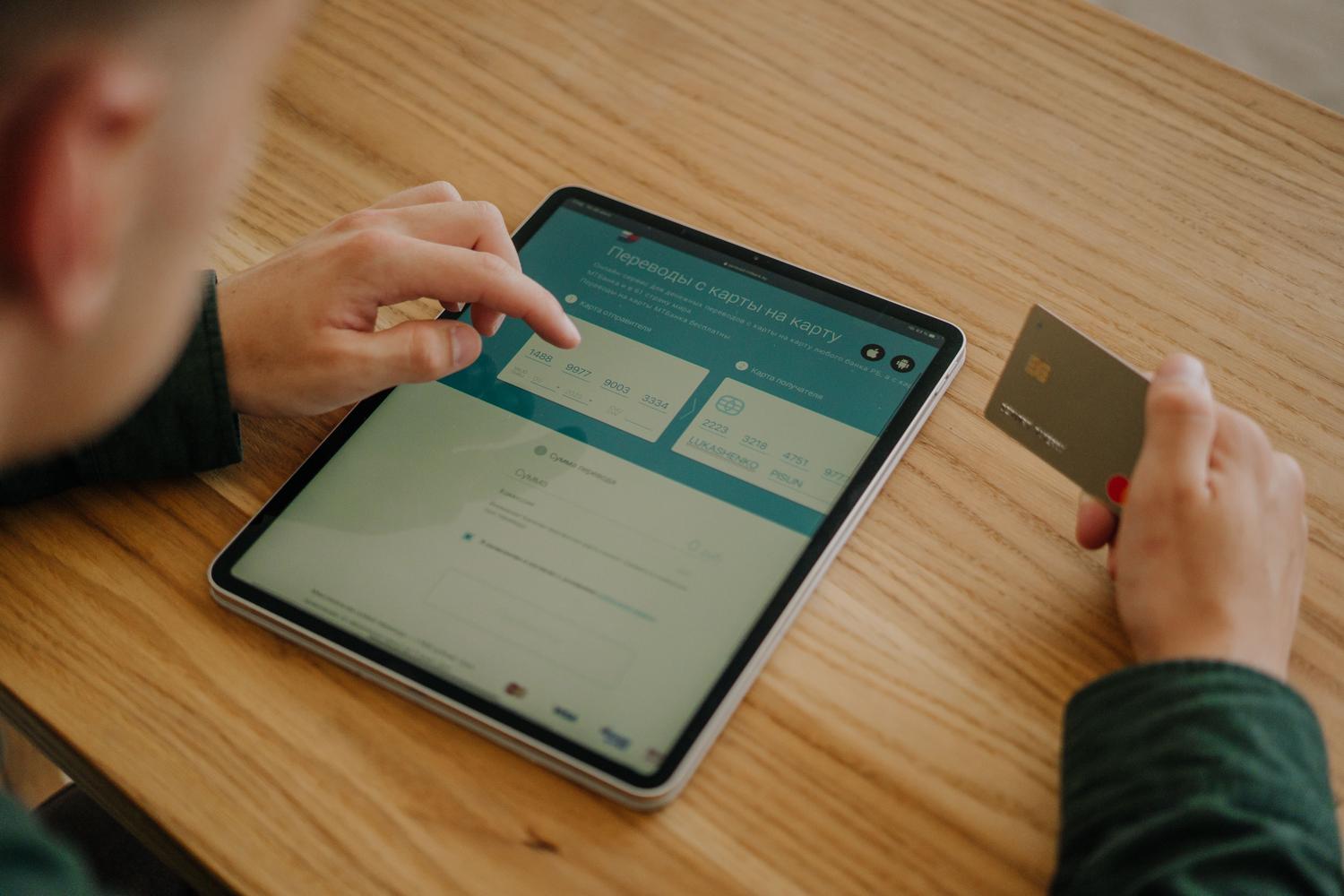 Persona realizando un pago online para un curso educativo utilizando una tablet y una tarjeta de crédito