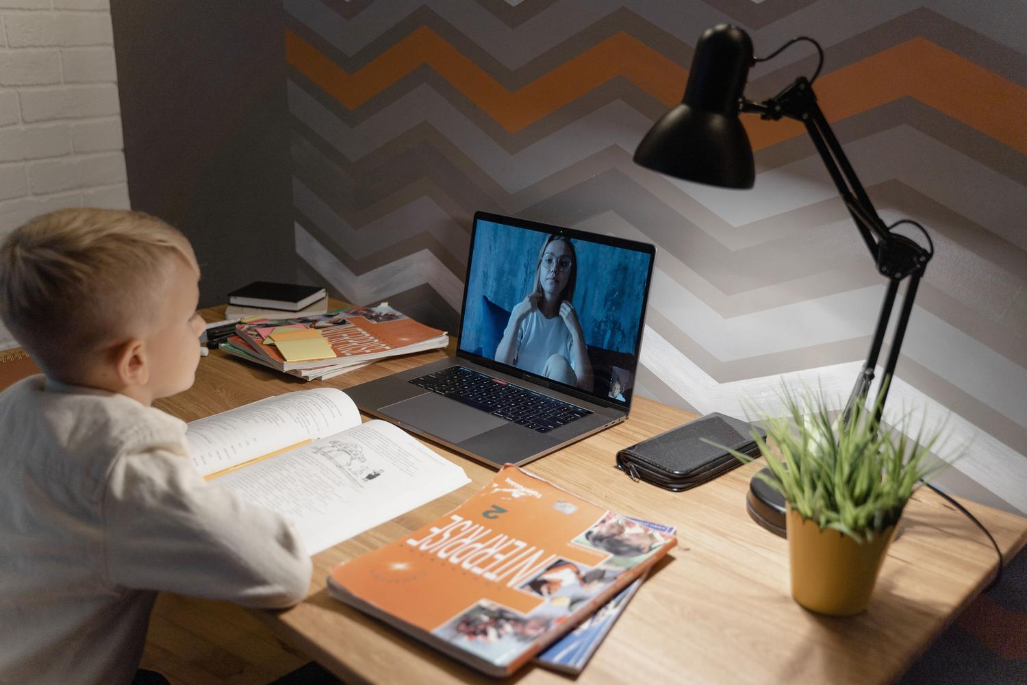 Estudiante participando en una clase virtual desde su hogar con materiales de estudio y un ordenador
