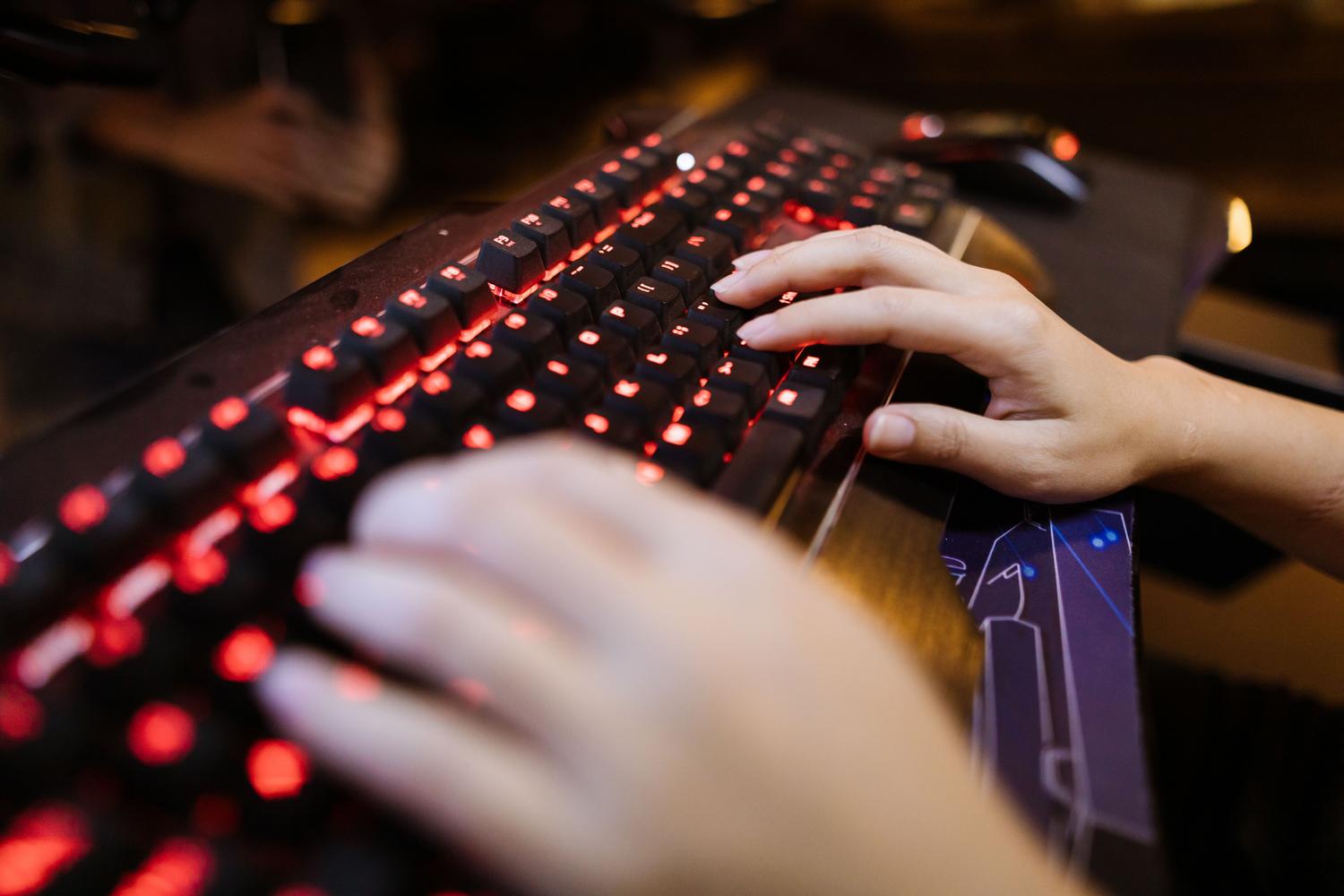 Primer plano de manos utilizando un teclado mecánico iluminado, sugiriendo un entorno de configuración técnica y optimización.