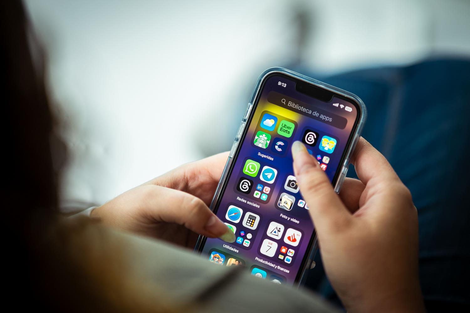 Primer plano de una persona sosteniendo un iPhone mostrando diversas aplicaciones en la pantalla