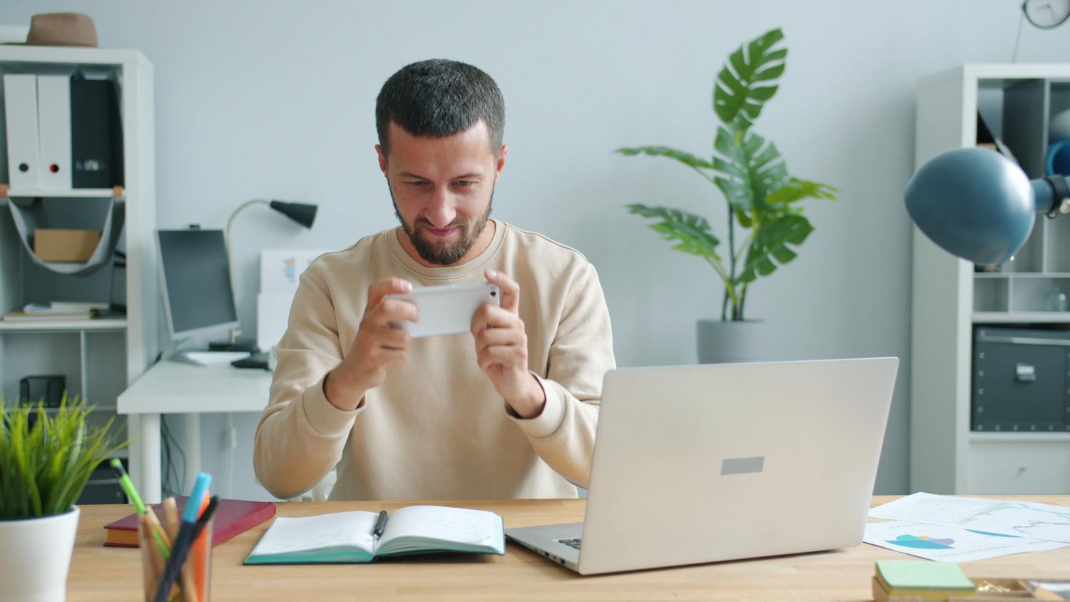 Profesional utilizando un smartphone en su escritorio de oficina junto a un ordenador portátil. Profesional utilizando un smartphone en su escritorio de oficina junto a un ordenador portátil.
