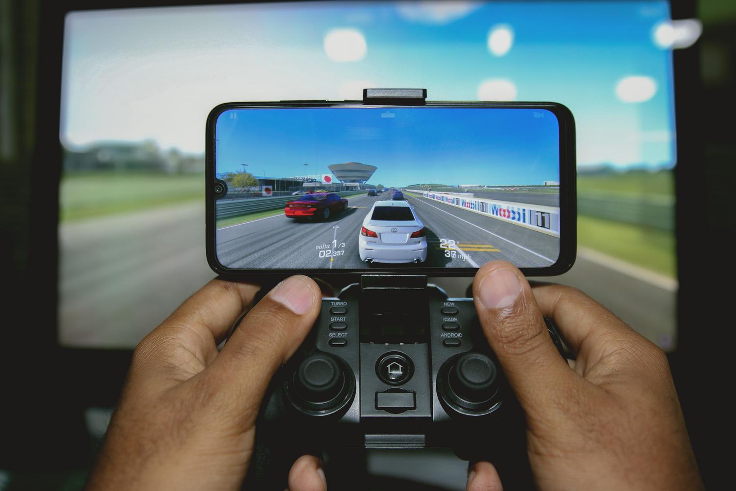 Primer plano de manos utilizando un mando de videojuegos bluetooth con un smartphone montado mostrando un juego de carreras.