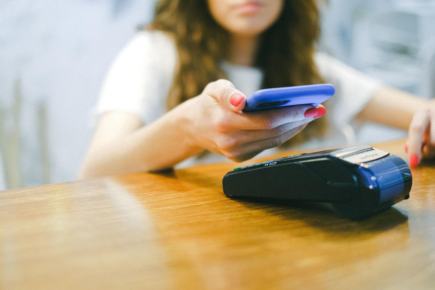 Mujer realizando un pago móvil sin contacto con su smartphone en un terminal de venta.