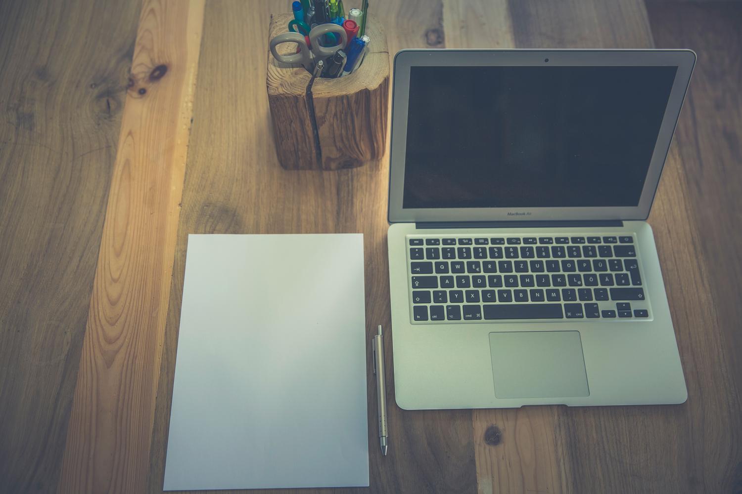 Escritorio minimalista de madera con un ordenador portátil, papel y material de oficina, transmitiendo orden y productividad.