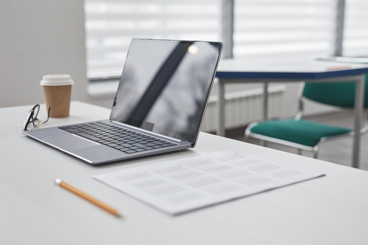 Espacio de trabajo moderno y limpio con un ordenador portátil, una taza de café y documentos impresos sobre un escritorio blanco.