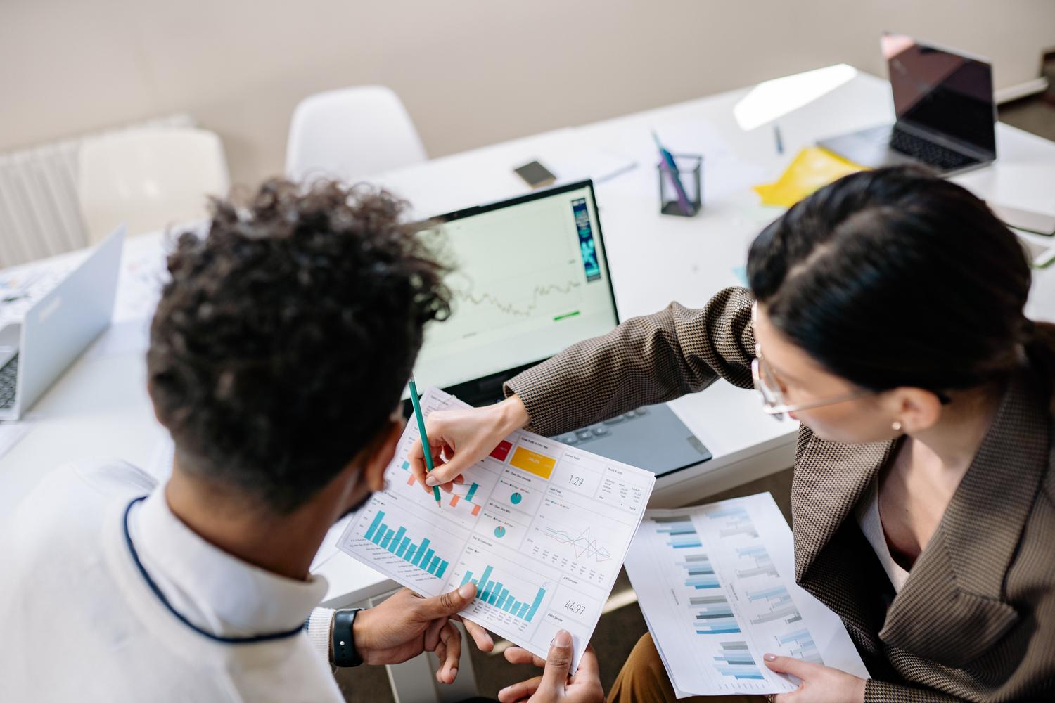 Dos colegas en una oficina analizando juntos gráficos de datos en un ordenador portátil para tomar decisiones estratégicas