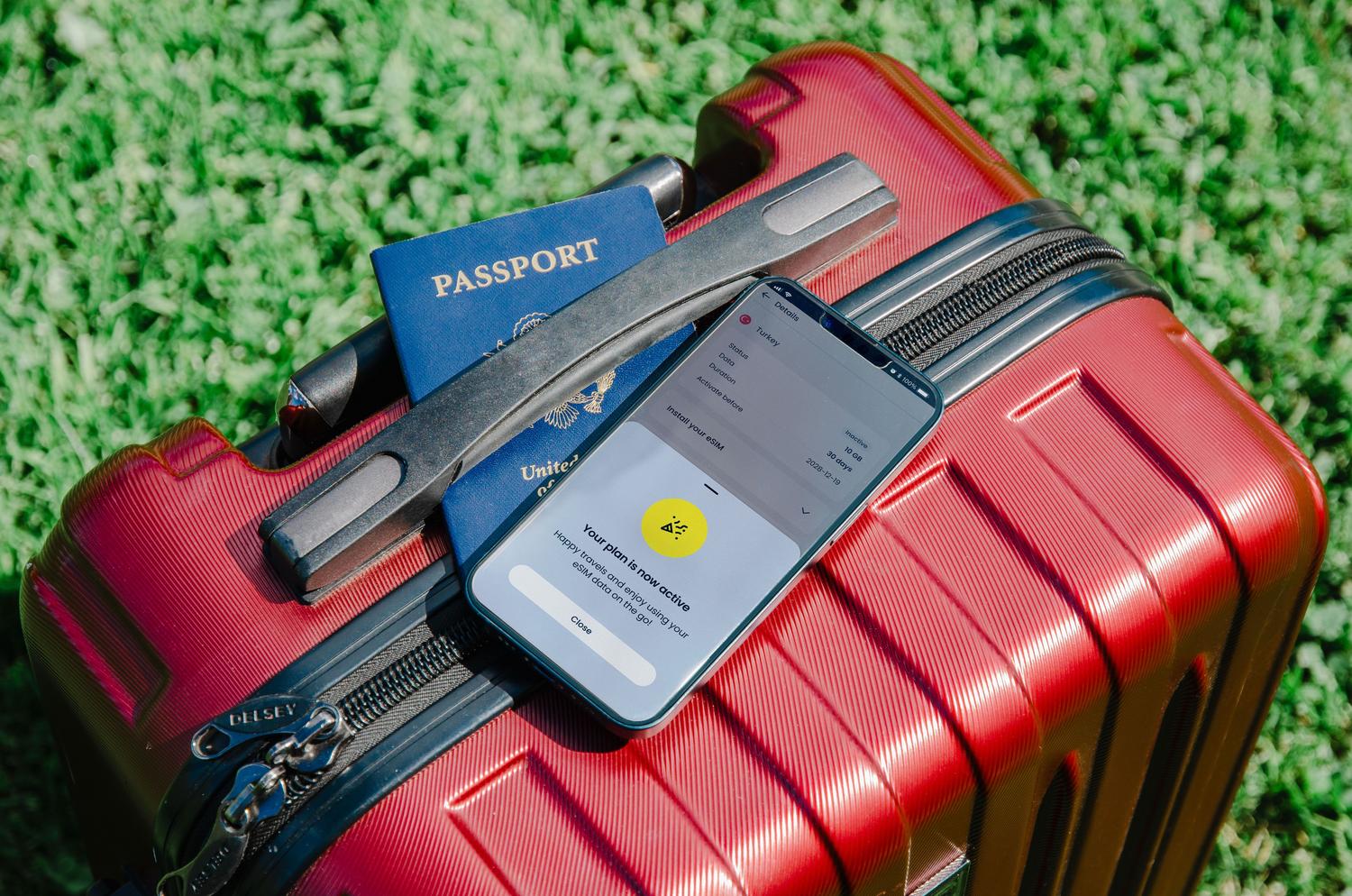 Primer plano de un pasaporte y un smartphone sobre una maleta roja, representando la gestión de documentos de viaje digitales.