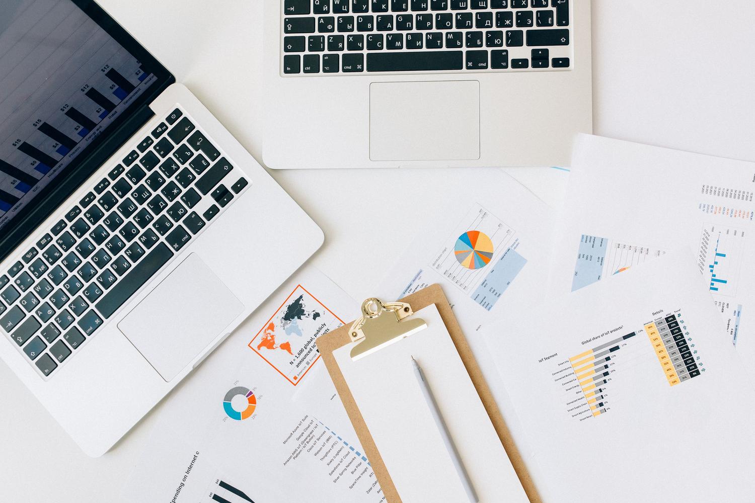 Vista cenital de portátiles, gráficos y reportes de datos sobre un escritorio, ideal para representar la productividad en la oficina.