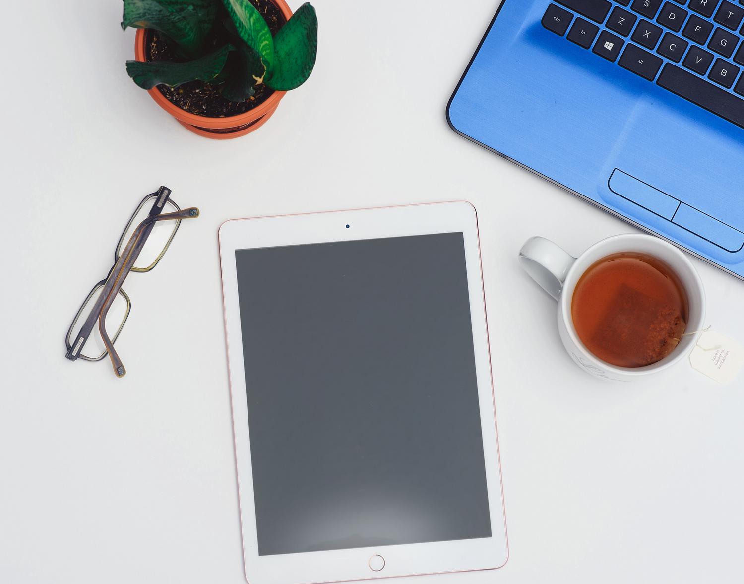 Escritorio minimalista y luminoso con un portátil, una tablet y una taza de té, evocando un ambiente de trabajo concentrado.