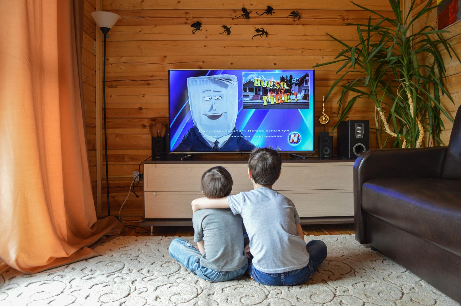 Dos niños sentados en el suelo viendo la televisión juntos, ilustrando el uso de AirPlay para compartir fotos y vídeos en familia.